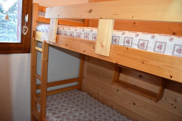 A bunk bed with a ladder, wooden walls, and patterned bedding.