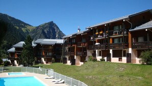 A hotel with multiple balconies, a swimming pool, and a mountainous backdrop.