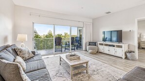 Ein geräumiges Wohnzimmer mit einer großen Schiebeglastür, die auf einen Balkon führt, einem Flachbildfernseher und einer gemütlichen Sitzecke.
