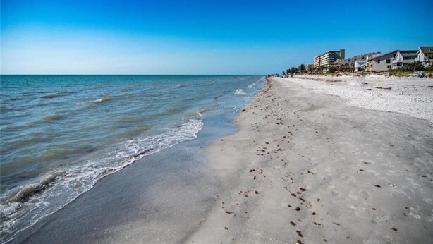 Ein Strand mit blauem Himmel, ruhiger See und Gebäuden im Hintergrund.