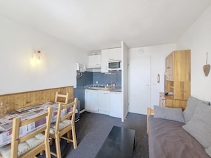Quarto compacto com mesa de jantar, cadeiras, sofá, cozinha compacta e um armário de madeira.