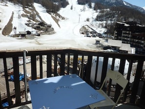 A view from a balcony overlooking a snowy ski slope with buildings and a chairlift in the background.