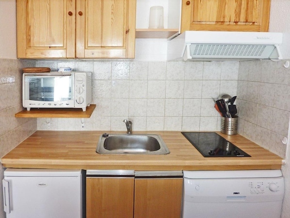 A compact kitchen with wooden cabinets, a microwave, a sink, and a dishwasher.