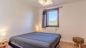 A bedroom with a bed, bedside lamps, a window with curtains, a radiator, and a small stool. - 50m from ski slopes, 4th floor, view mountain, balcony, tv, ski locker, 36m², La Plagne (La Plagne)