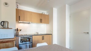 A compact kitchen with wooden cabinets, a built-in oven, and a microwave. There is a dining table with a patterned tablecloth and a white chair. - 50m from ski slopes, 4th floor, view mountain, balcony, tv, ski locker, 36m², La Plagne (La Plagne)