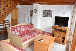 A cozy living room with a wooden sofa, a television on a wooden stand, and a staircase leading to another room.