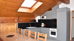 Una cocina compacta con vigas de madera en el techo, tragaluz, gabinetes grises, microondas, cafetera y estufa.