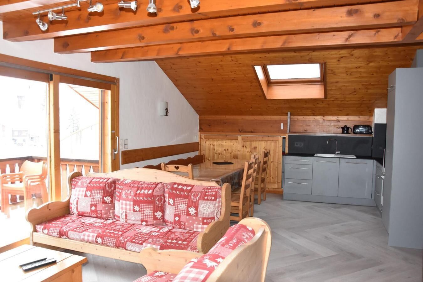 Un acogedor interior de cabaña con techo de madera, un comedor con mesa y sillas, una kitchenette y un sofá con funda estampada.