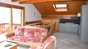 Un acogedor interior de cabaña con techo de madera, un comedor con mesa y sillas, una kitchenette y un sofá con funda estampada.