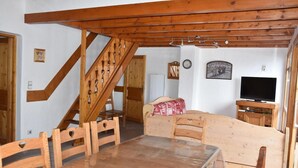Una habitación acogedora con una escalera de madera, una mesa de comedor con sillas, una cama, un televisor y un reloj en la pared.