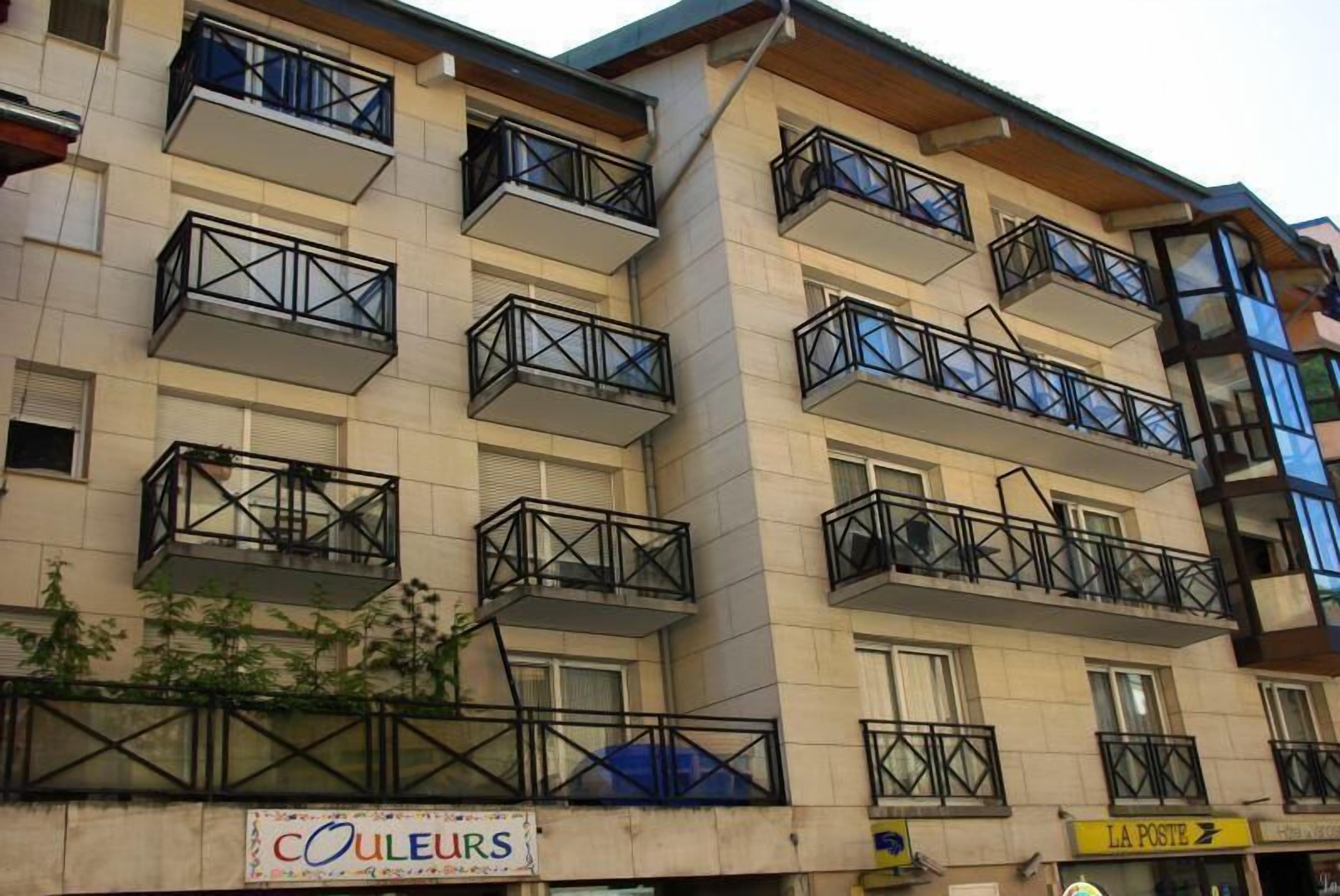 A multi-story building with balconies, a sign for 'COULEURS', and a 'LA POSTE' shop.