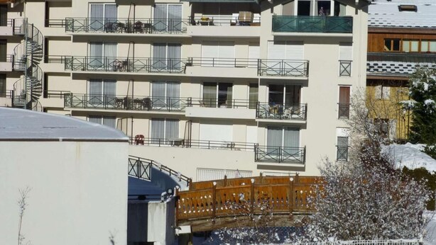 Ein mehrgeschossiges Gebäude mit Balkonen, vermutlich ein Hotel oder eine Wohnanlage, mit Schnee auf dem Dach und in der Umgebung.