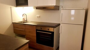 Eine kleine Küche mit Spüle aus Edelstahl, eingebautem Backofen und einem weißen Kühlschrank.