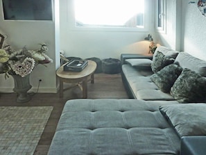 Ein Wohnzimmer mit einem grauen Sofa, einem kleinen runden Tisch und einer Blumenvase.
