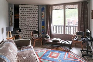 A cozy living room with a sofa, two chairs, a small table, and a computer setup.
