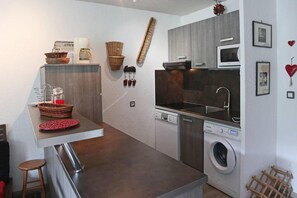 Une cuisine compacte équipée d’un lave-linge intégré, d’une machine à café et d’un four à micro-ondes.