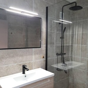 A modern bathroom with a glass-enclosed shower, a white sink, and a large mirror.