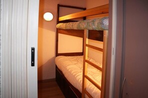 Un lit superposé avec un matelas et une tête de lit, une porte avec une poignée et un luminaire fixé au mur.
