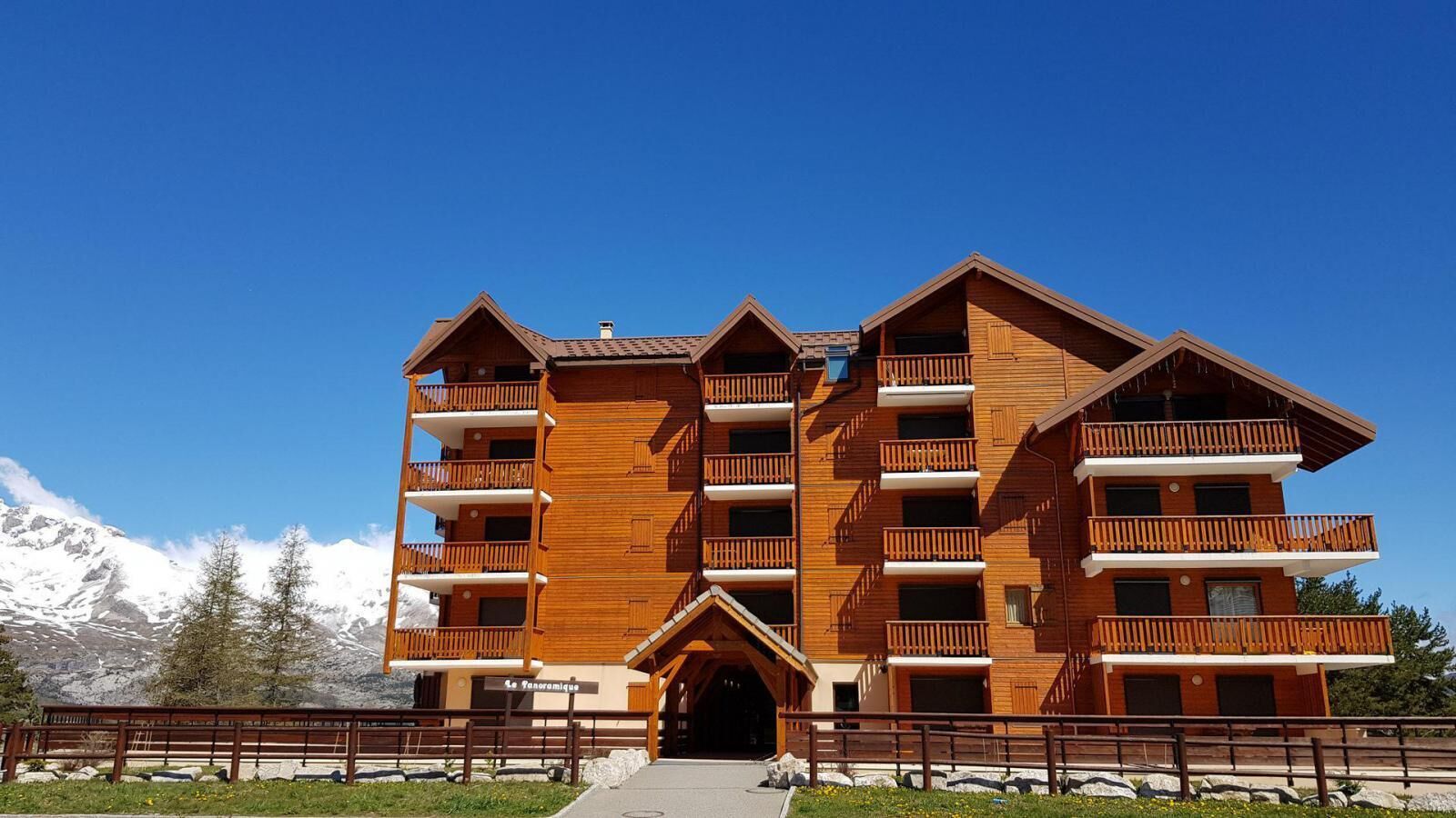 A multi-story wooden building with balconies, a central entrance, and a mountainous backdrop.