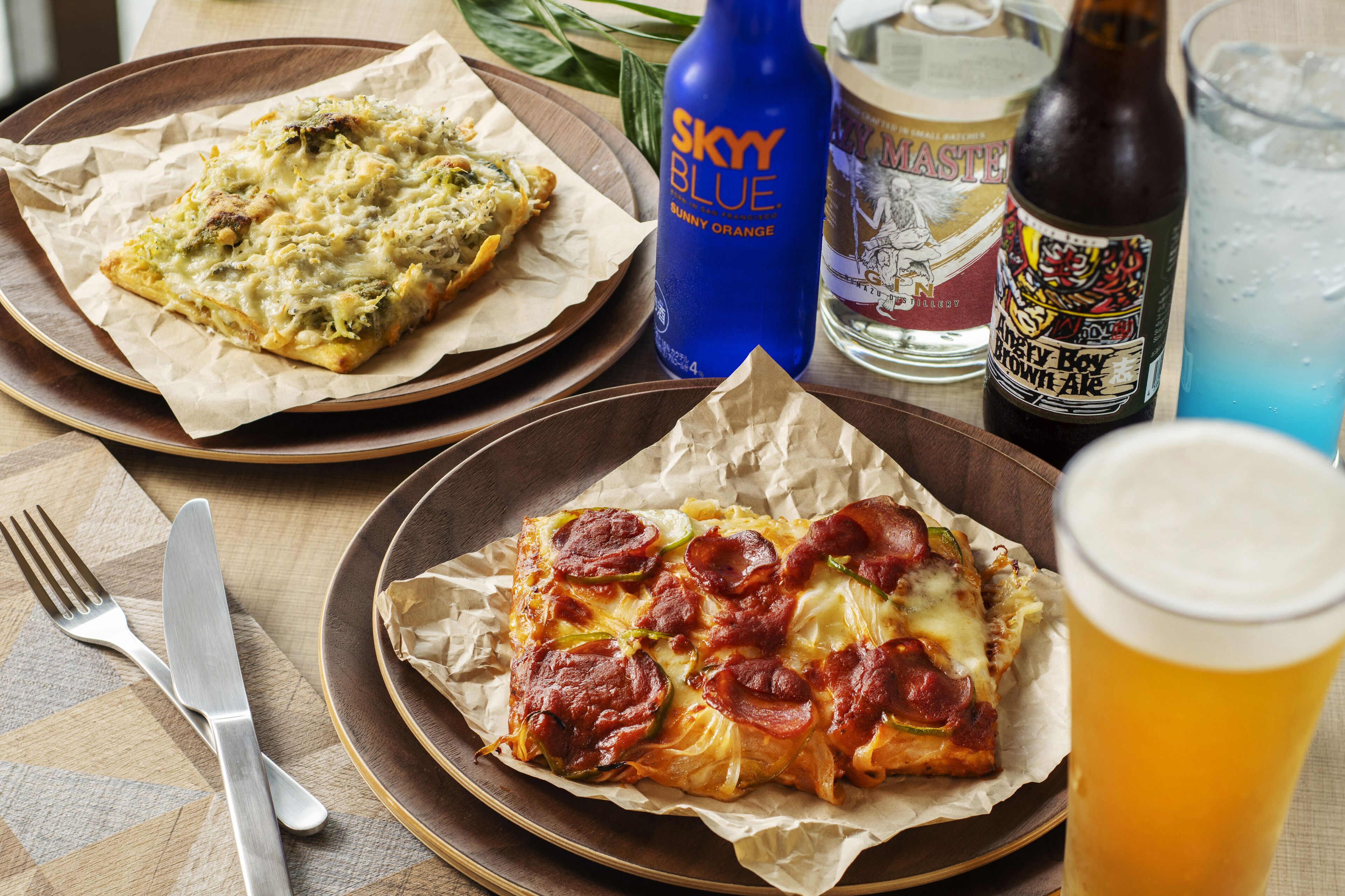 Duas pizzas em pratos, uma garrafa de cerveja e um copo de cerveja.