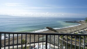 A coastal view from a balcony overlooking a beach with a rocky breakwater, a parking area, and a clear sky. - Atagawa Ocean Resort (Higashiizu)