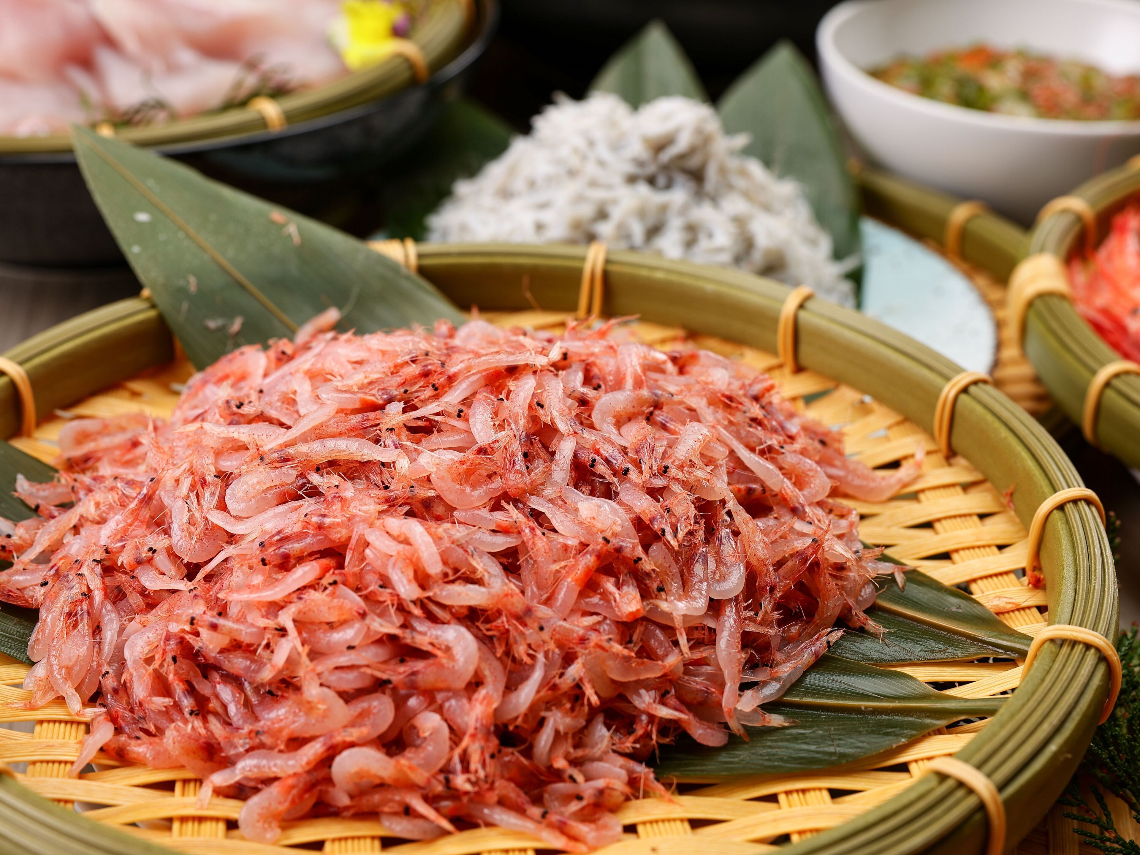 Una mesa con una gran pila de camarones crudos sobre una bandeja tejida.