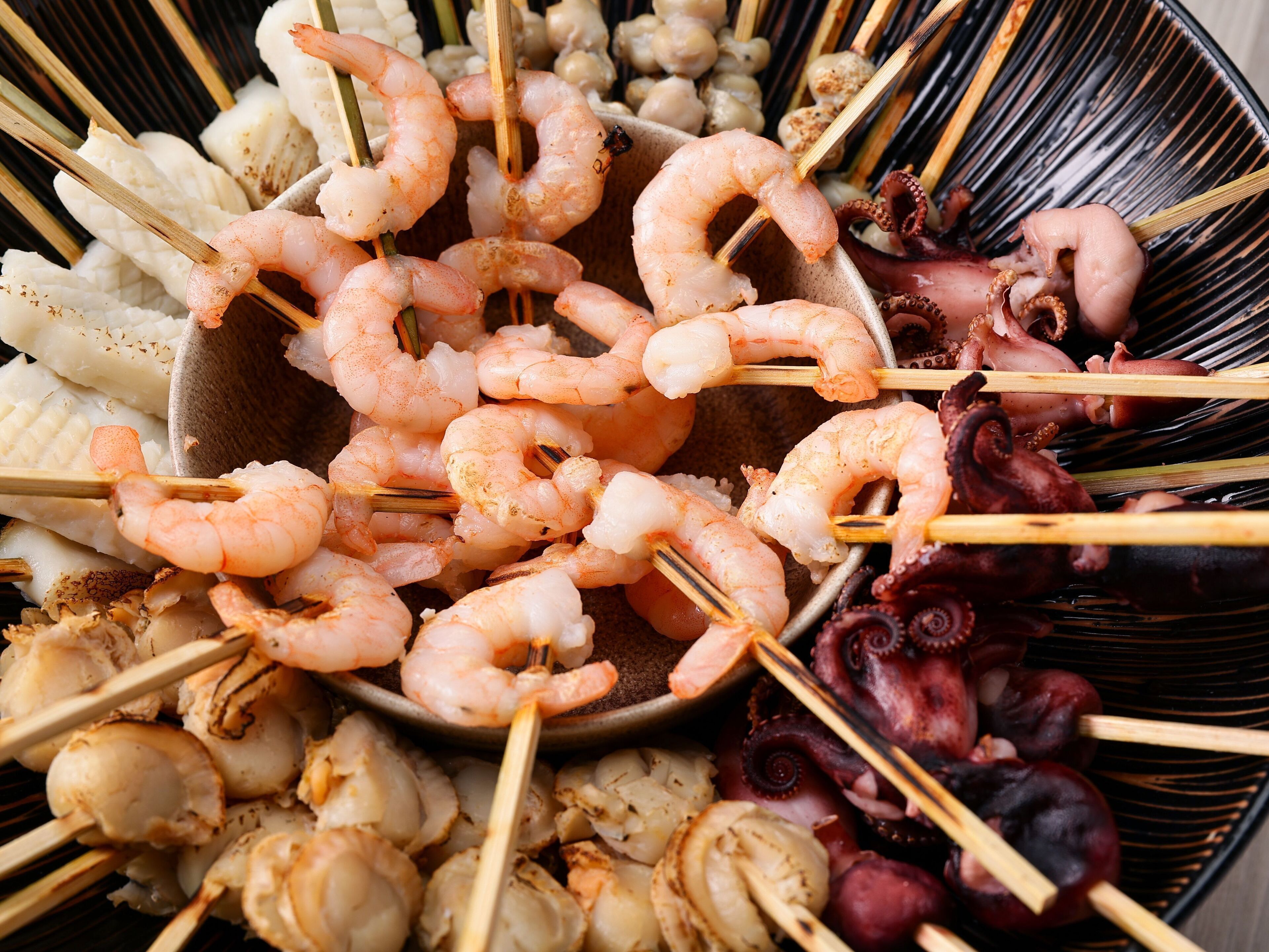 Un tazón con brochetas variadas de mariscos, incluyendo camarones, calamares y pulpo.