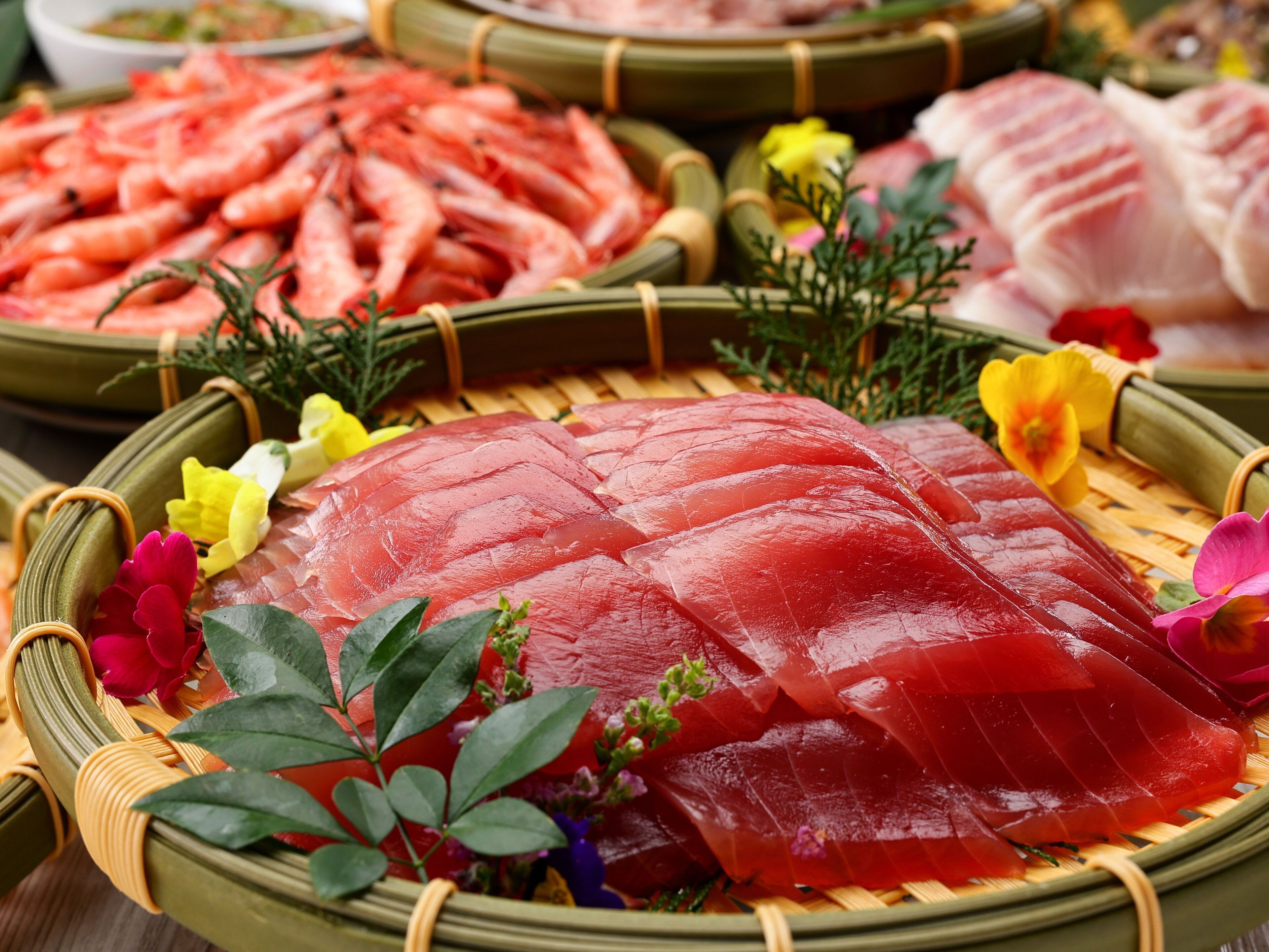 A variety of fresh seafood including shrimp and sashimi on woven baskets.