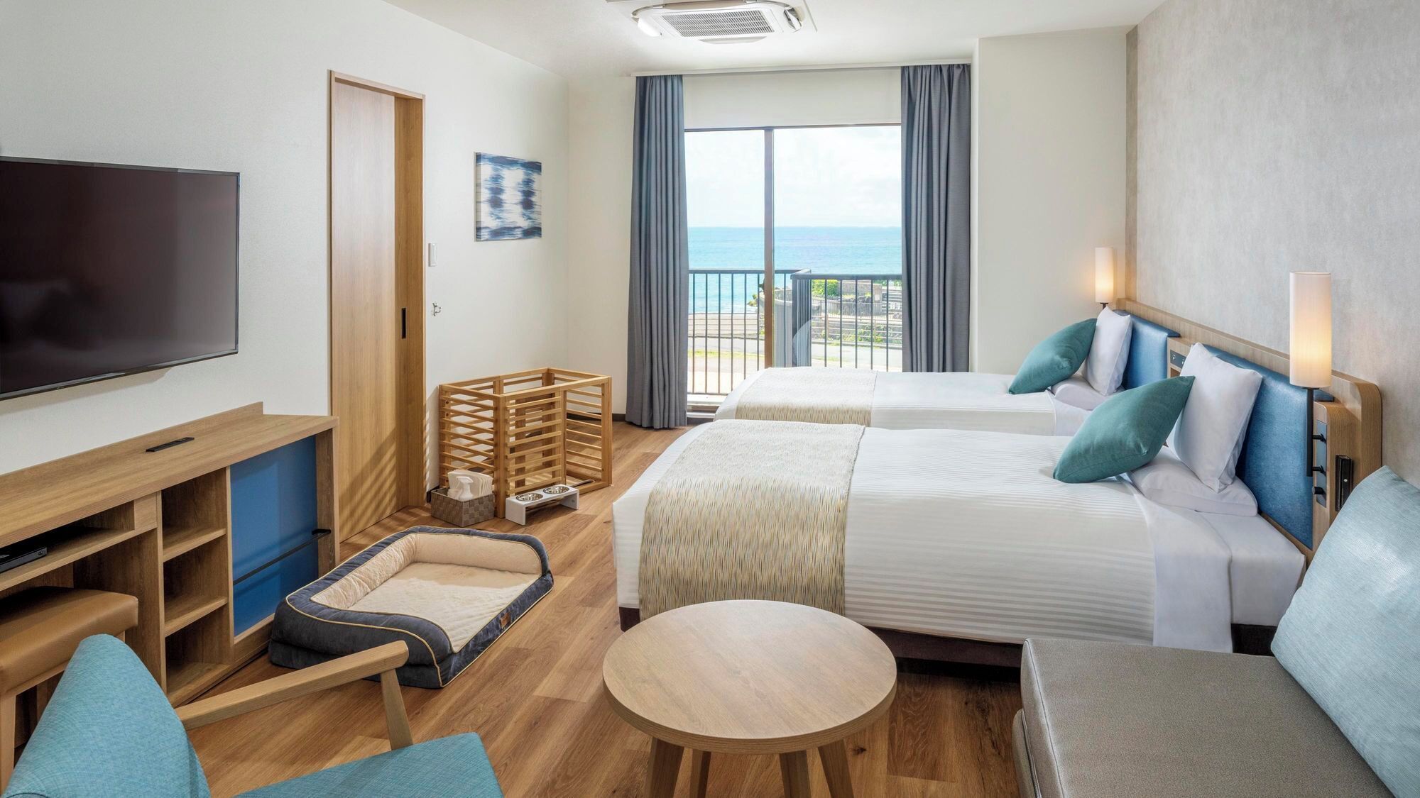 A hotel room with two beds, a TV, a desk, a small table, and a balcony with a view.