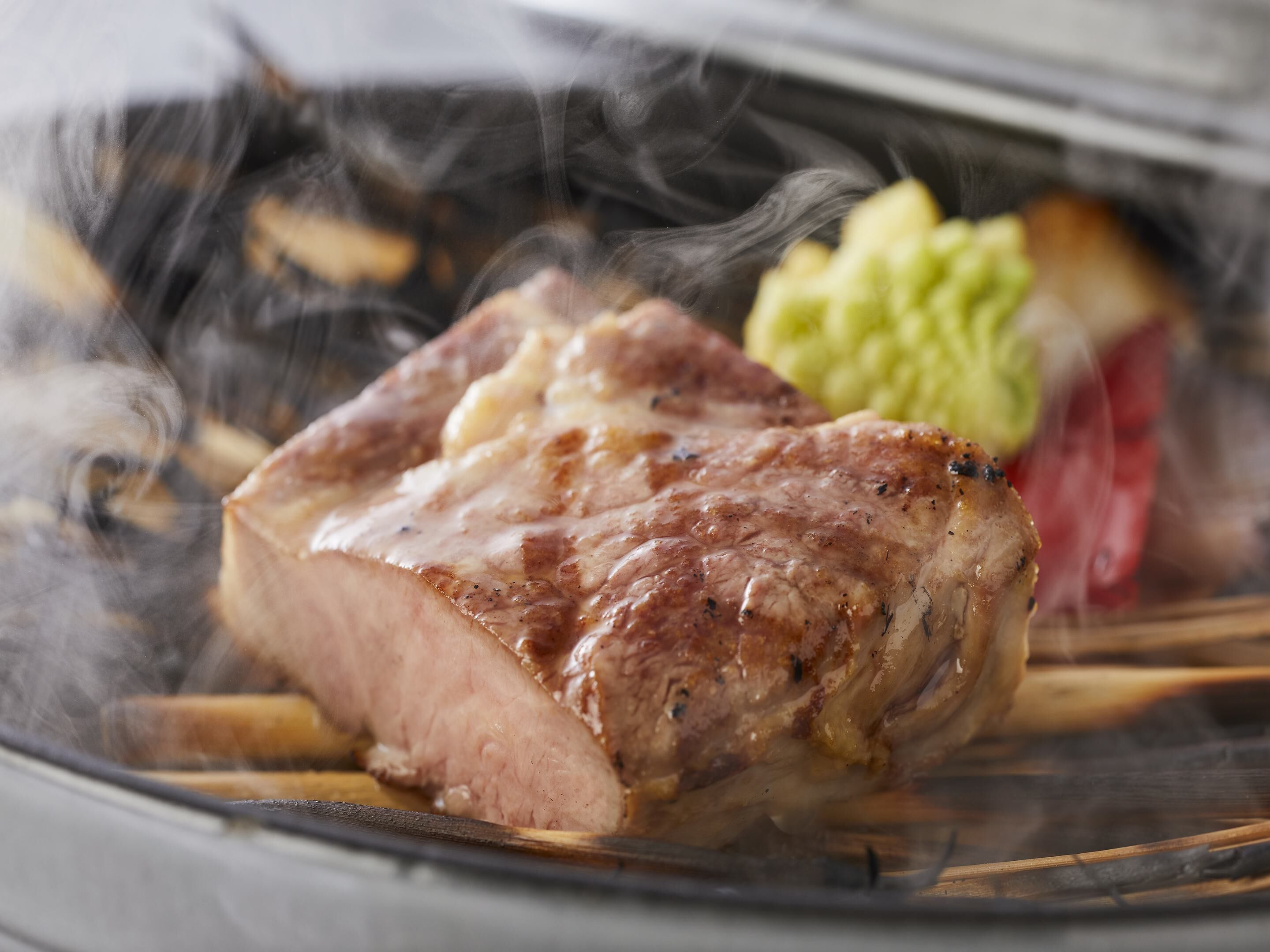 A grilled steak with a side of vegetables and a slice of red meat, possibly a steak or roast, on a plate.