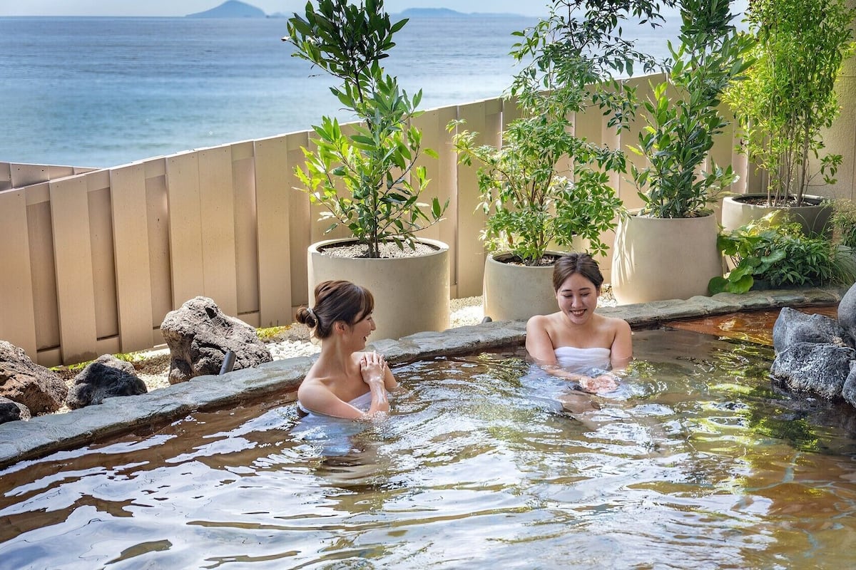 Una piscina de hidromasaje con vistas al mar, rodeada de plantas en macetas y una cascada de piedra.