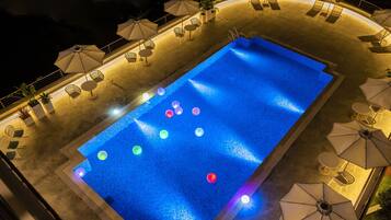 Piscina com deck ladrilhado, rodeada por espreguiçadeiras e guarda-sóis.
