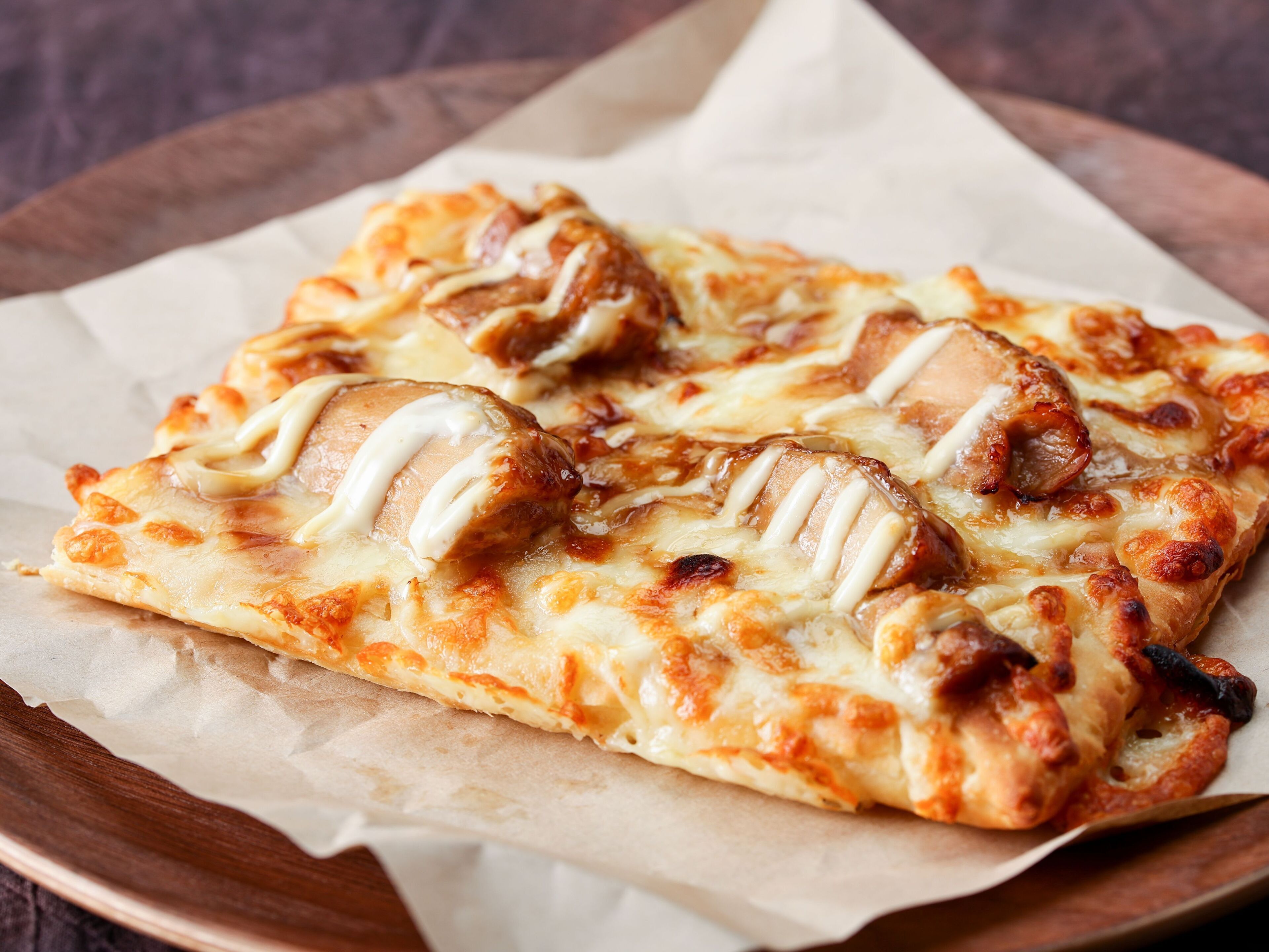 Eine Pizza mit Käse und Belag auf einem Holzbrett.