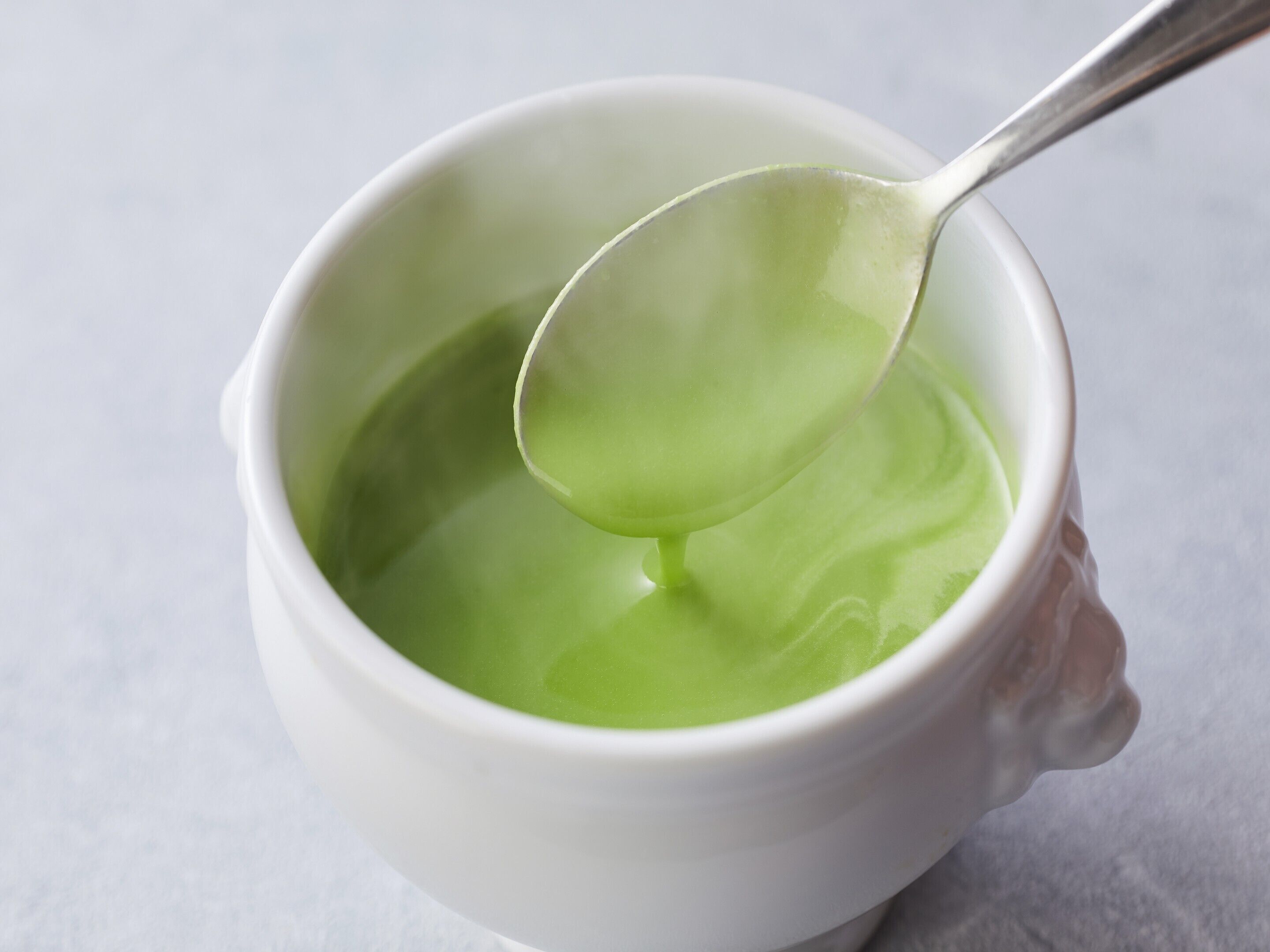 Una taza de cerámica blanca con una cuchara en su interior, conteniendo un líquido verde.