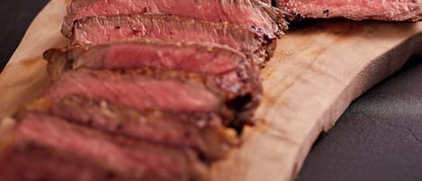 A wooden board with sliced meat and rosemary.