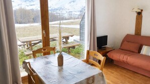 A room with a wooden table and chairs, a sofa, a TV, and a view of snow-capped mountains. - Ground floor, view mountain, swimming pool, terrace, parking, tv, ski locker, 25m², La Joue du Loup (Agnières-en-Dévoluy)