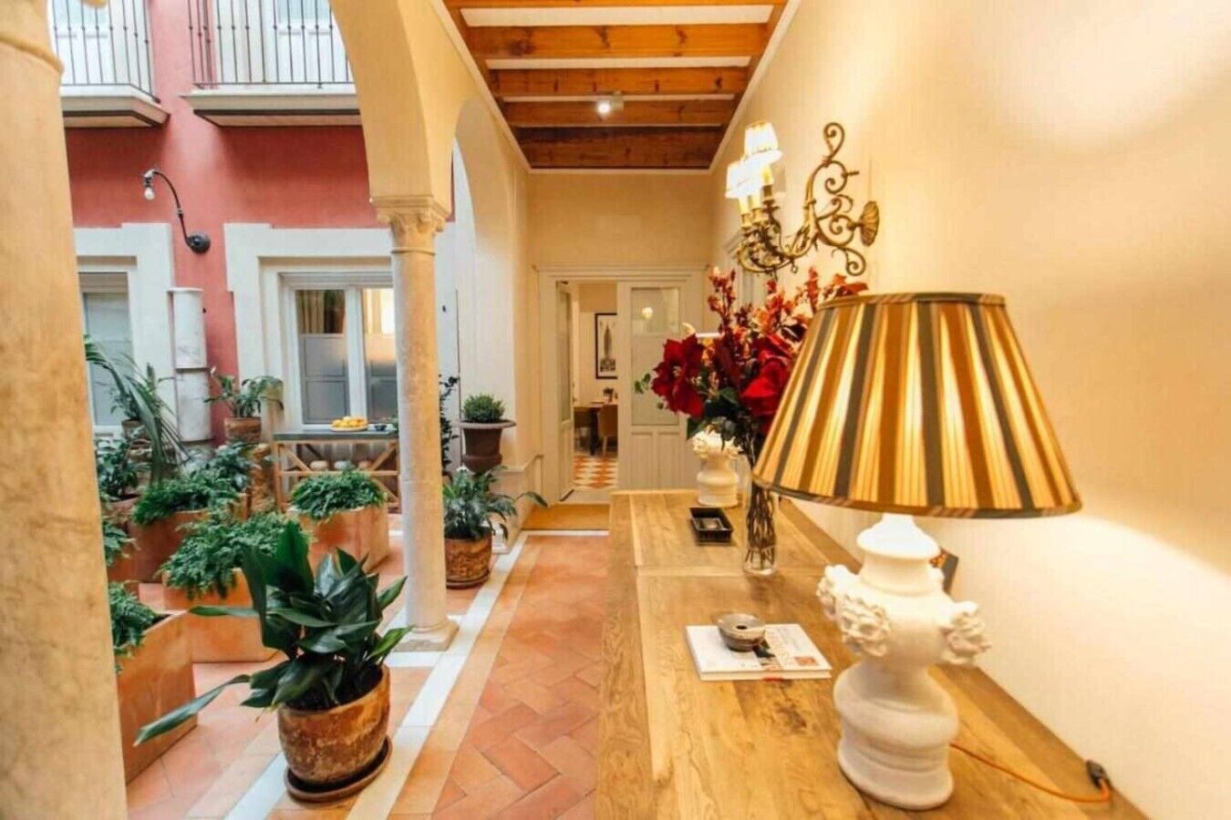 A corridor with a wooden floor, potted plants, a white lamp, and a door leading to another room.