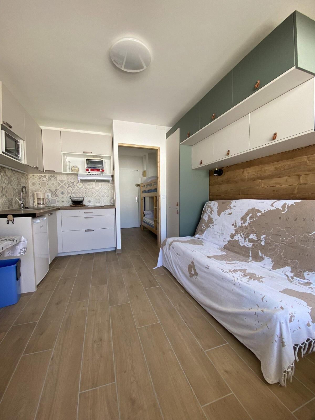 A compact room with a kitchenette, a bed, and a wooden floor.