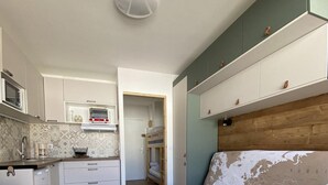 Pieni huone, jossa on pieni keittiönurkkaus, sänky ja puulattia.