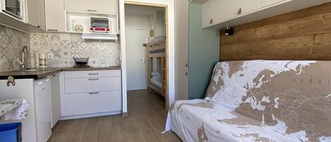 A compact room with a kitchenette, a bed, and a wooden floor.