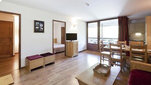 Habitació petita amb llit, televisió, taula de dinar amb cadires i un balcó amb vistes.