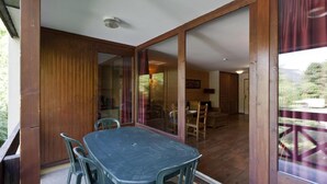 Habitació amb taula i cadires de fusta, una porta corredissa de vidre que dona a un balcó i vista a un vehicle a l'exterior.