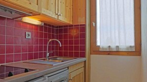 Ett kompakt kök med en diskho i rostfritt stål, träskåp och röda kakelplattor.