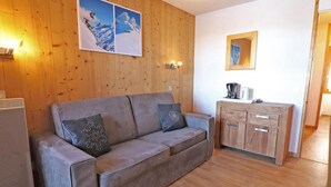 Ett rum med träpanel på väggarna, en grå soffa, två kuddar, ett träskåp och en inramad tavla på väggen.