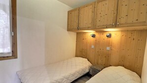 Quarto pequeno com duas camas, paredes de painel de madeira e iluminação embutida.