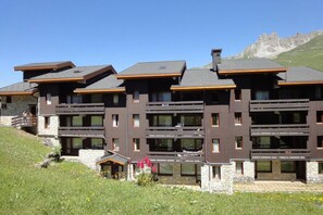 Un hotel a più piani con balconi, facciata in pietra e montagne sullo sfondo.
