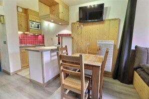 Una cucina compatta con mobili in legno, un forno a microonde, una TV e un'area pranzo con tavolo e sedie.