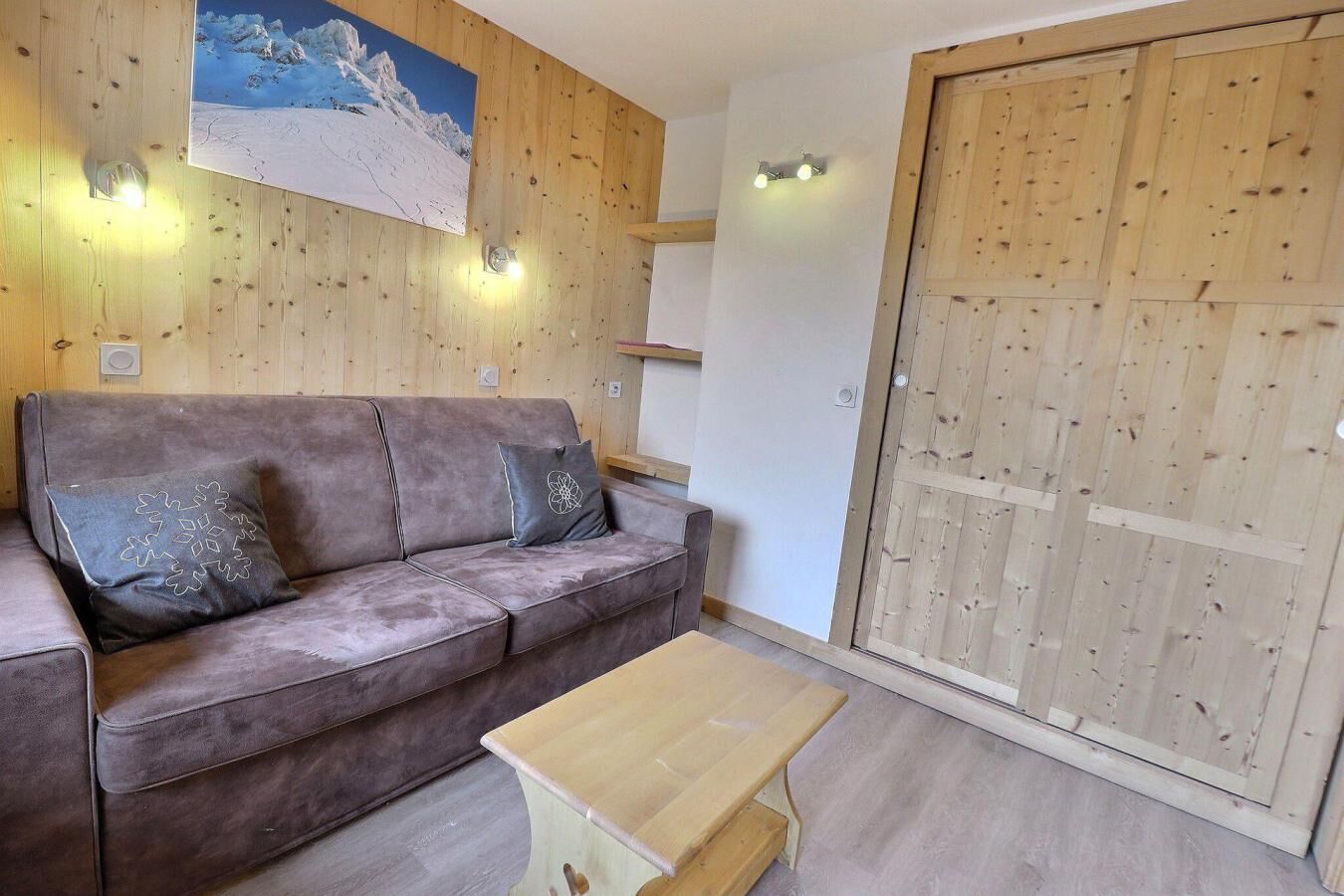 Une pièce chaleureuse avec un mur en bois, un canapé avec des coussins, une petite table en bois et une grande porte en bois.