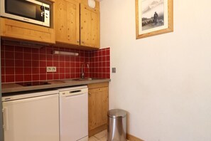 A compact kitchen with wooden cabinets, a microwave, a dishwasher, and a sink. - 10m from ski slopes, 5th floor, balcony, ski locker, 20m², Méribel-Mottaret (Méribel - Les Allues)