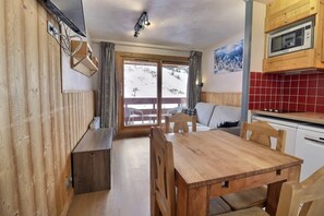 A wooden interior with a dining table and chairs, a kitchen with a microwave, and a view of a snowy landscape through a glass door.